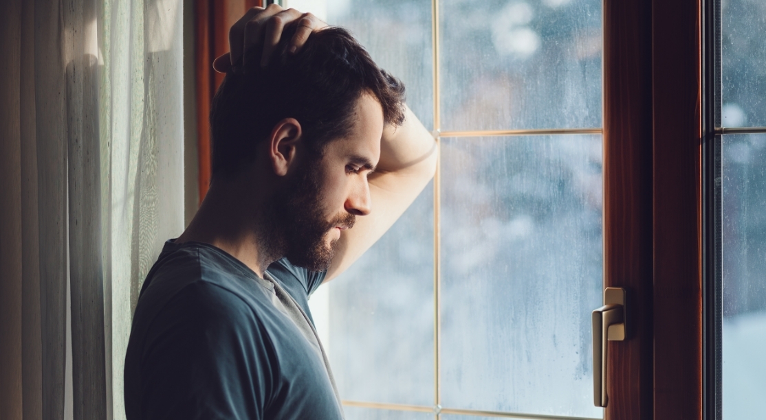 Man holding his head looking out the window